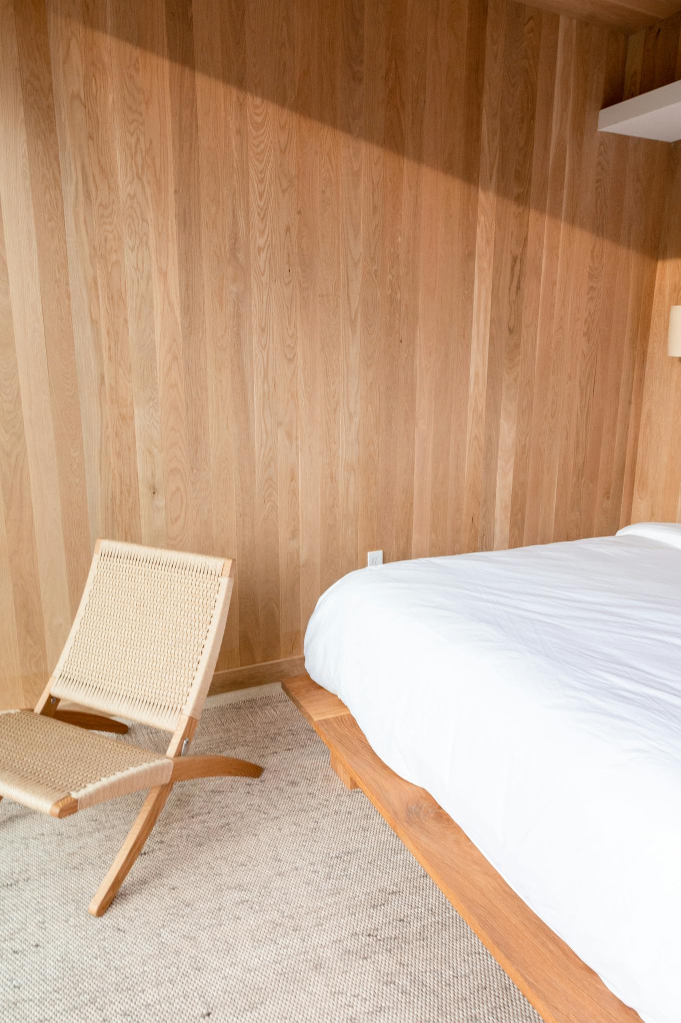 Bright minimalist bedroom with wooden walls and modern chair, perfect for relaxation.